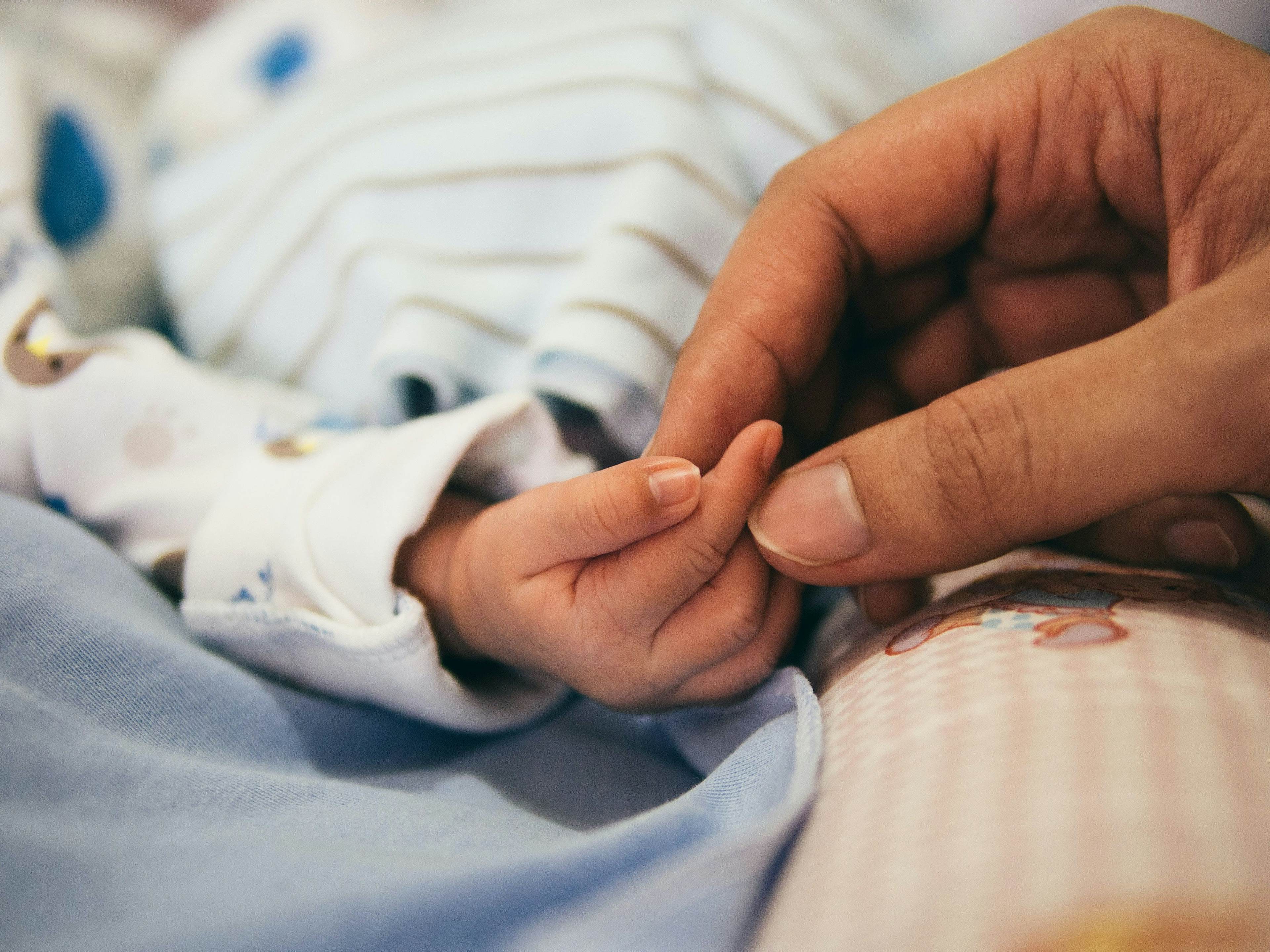 Newborn baby grasping finger of caregiver