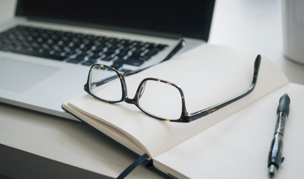 laptop next to notebook and glasses