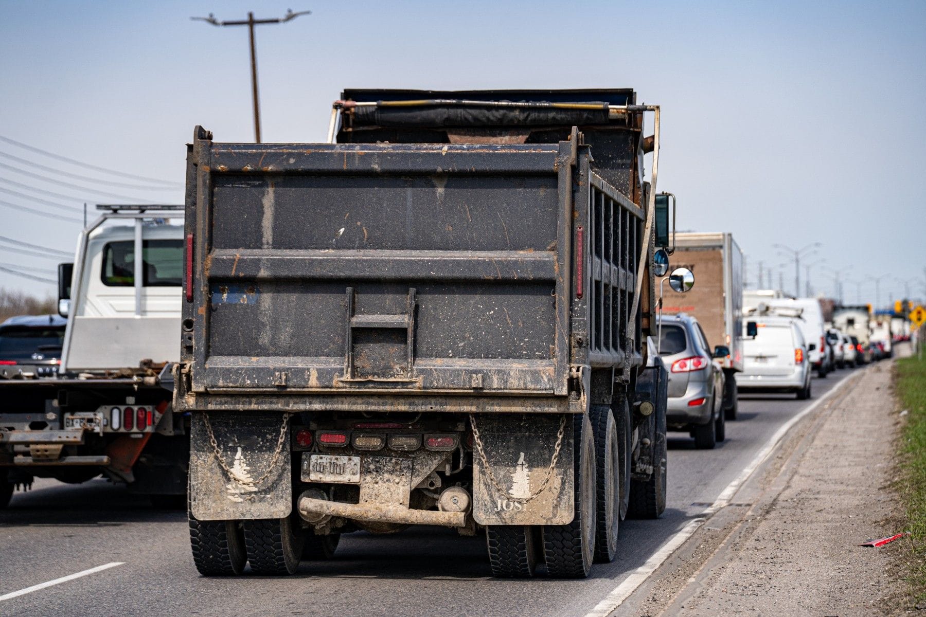 A dump truck travels on a busy road, with several cars and trucks queued in front of it.